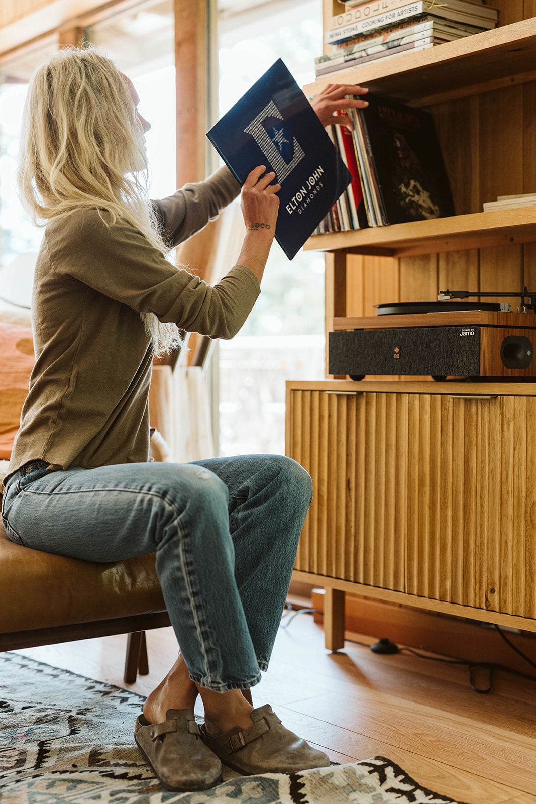 Woman in a casual olive long sleeve tee selects a record in a cozy home setting
