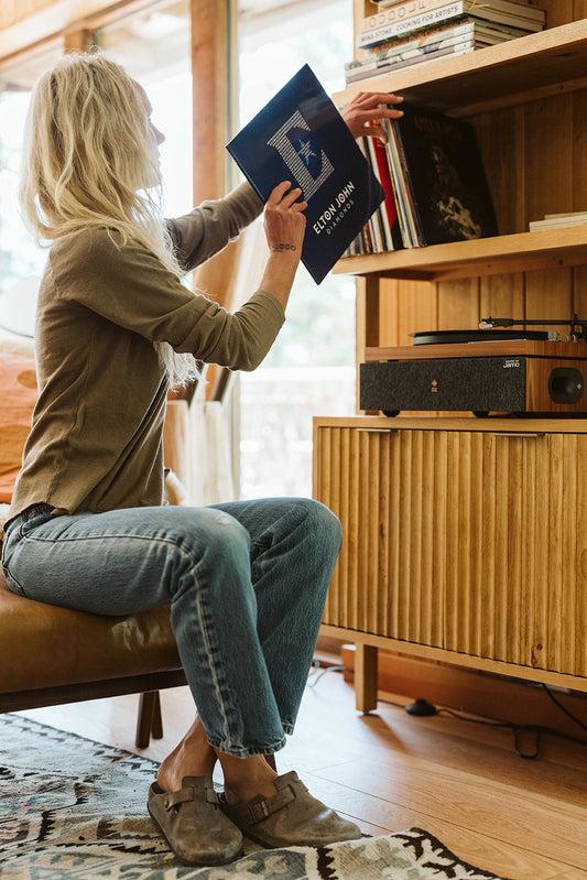 Woman in a casual olive long sleeve tee selects a record in a cozy home setting