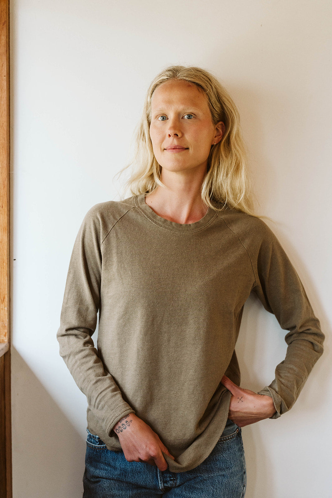 Woman in an olive long sleeve tee and jeans standing against a light wall