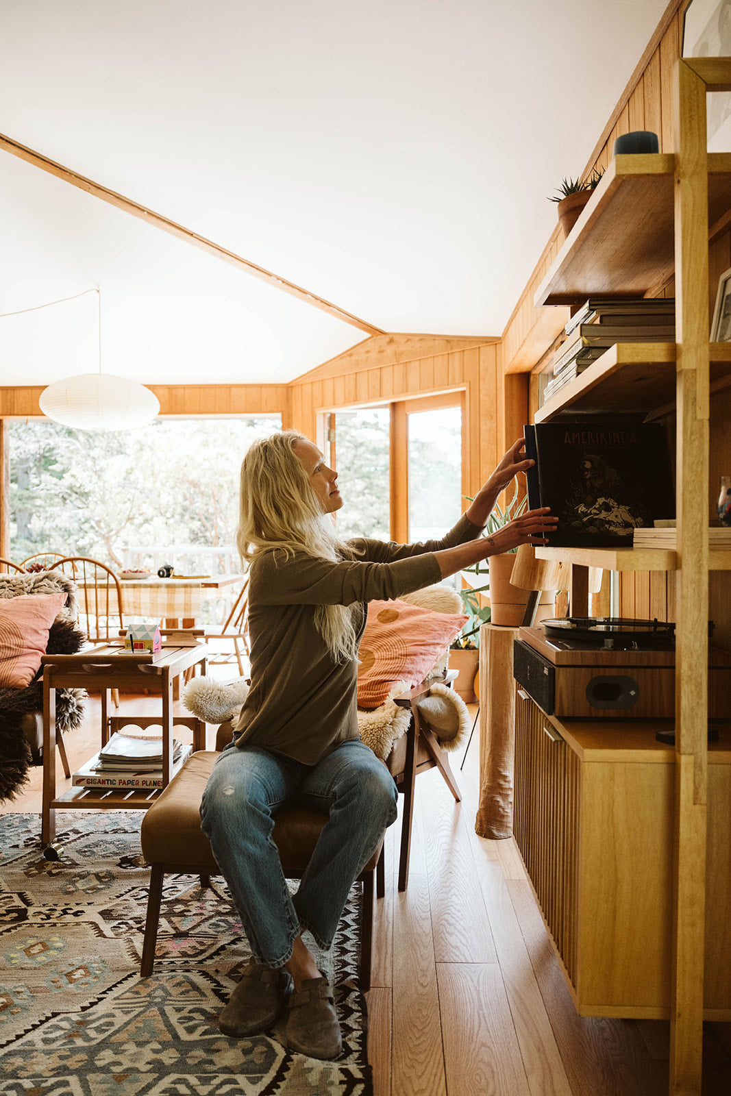 Woman in an olive long sleeve tee sorts vinyl records in a bright, inviting living room